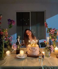 a woman sitting at a table in front of a cake with lit candles on it