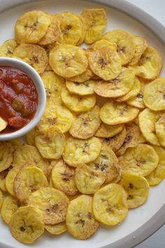 a white plate topped with sliced bananas and ketchup on top of it next to a bowl of chips