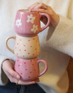 a woman holding three coffee mugs in her hands with hearts and flowers on them