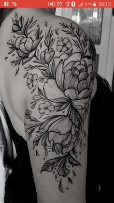 a woman's shoulder with flowers and leaves tattooed on her left arm, in black and white