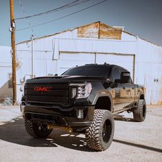 a large black truck parked in front of a white building with power lines above it