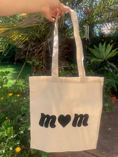 a person holding up a white bag with the word mom written in black on it