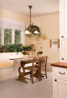 a dining room table and chairs in front of a window with potted plants on the windowsill