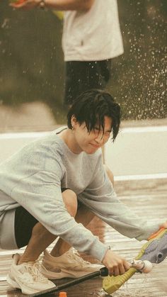 a young man is playing in the rain with an umbrella and water skis as he crouches down