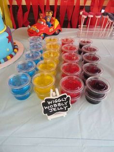 a table topped with lots of plastic cups filled with different colored liquids next to a cake