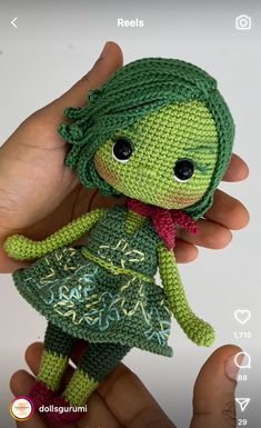 a crocheted doll in a green dress holding it's head with one hand