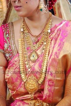 a woman in a pink and gold saree with jewelry on her neck, sitting down