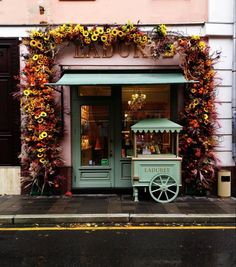 an old fashioned ice cream cart in front of a flower covered building with flowers all over it