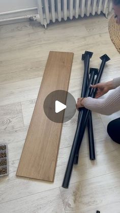 a woman sitting on the floor with some sticks in front of her and another person kneeling down next to them