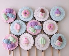 cupcakes decorated with pastel icing and candies are arranged on wooden sticks