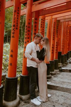 a man and woman standing next to each other in front of tall orange pillars