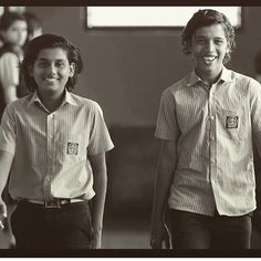 two young boys in school uniforms walking down the street with their hands behind their backs