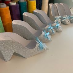 several pairs of glittered shoes with bows are lined up on a table next to spools of thread