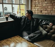 a man sitting on top of a brown couch next to a wooden table in front of a window