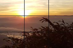 the sun is setting over some mountains and clouds in the sky as seen from a window