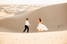 a man and woman are running in the sand dunes with their arms around each other