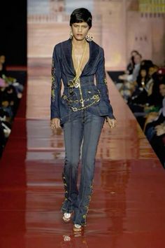 a woman walking down a runway wearing a blue suit and gold jewelry on top of her head