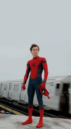 a man dressed as spider - man stands on a platform in front of a train