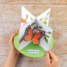 someone holding up a paper butterfly on top of a green plate with trees and leaves