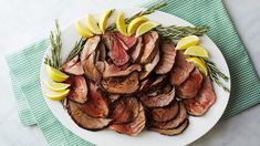 a white plate topped with sliced meat and lemon wedges on top of a table