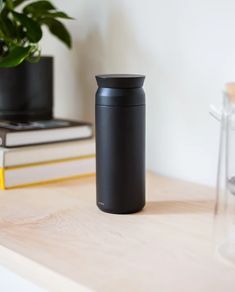 a black coffee cup sitting on top of a wooden table next to some books and a potted plant