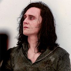 a man with long black hair wearing a green shirt and looking off into the distance