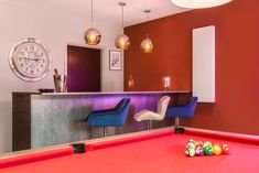 a pool table in a room with two chairs and a clock on the wall behind it