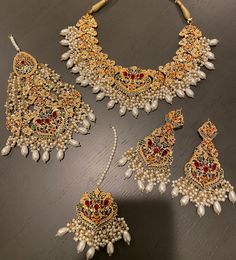 an elaborate necklace and earring set with pearls, rubs and stones on a wooden surface