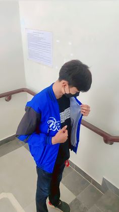 a young boy wearing a blue jacket looking at his cell phone while standing on the stairs