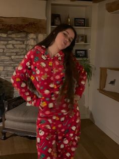 a woman standing in front of a fire place wearing red pajamas and smiling at the camera