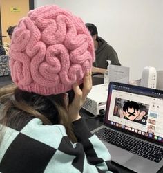 a woman sitting at a table with a laptop and a pink brain hat on her head