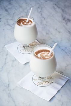 two glasses filled with liquid sitting on top of a white napkin next to each other