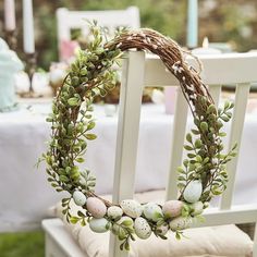 a white chair with an easter wreath on it and eggs in the middle sitting next to a table