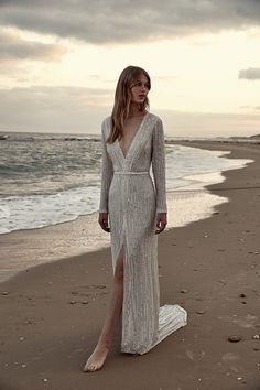 a woman standing on top of a sandy beach next to the ocean wearing a silver dress