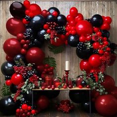 a table topped with lots of red and black balloons next to a wall covered in greenery