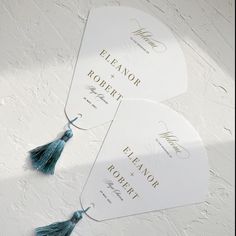 two white fan shaped tags with tassels on them sitting next to each other