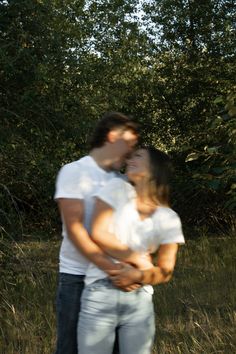 a man and woman standing next to each other in front of some trees on a sunny day