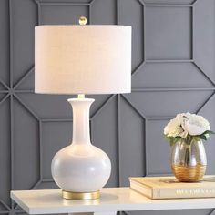 a white table lamp sitting on top of a desk next to a vase with flowers