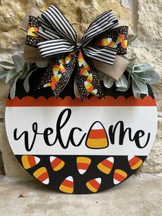 a welcome sign hanging on the side of a stone wall with leaves and candy corn