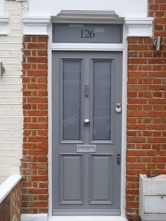 the front door is painted gray and has two windows on each side, along with a brick wall