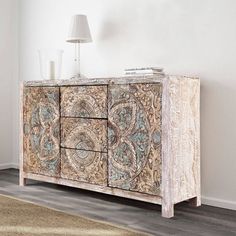 an ornately decorated sideboard with two drawers and a lamp on the table next to it