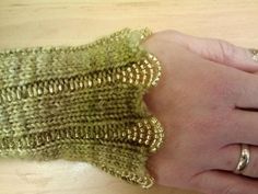 a woman's hand with gold rings on it holding a green knitted glove