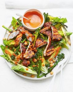 a white plate topped with lettuce and chicken next to a bowl of sauce