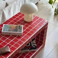 a red table topped with books and a mushroom lamp next to a white couch in a living room