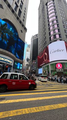 a red taxi cab driving down a street next to tall buildings with advertisements on them