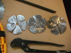 several tools are laying on a table next to some metal flowers and pliers with holes in them