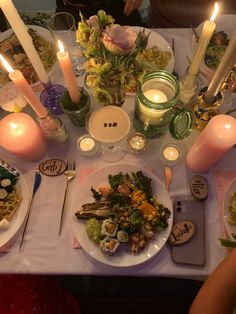 a dinner table with candles and plates of food on it, including salad or pasta