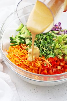 someone pouring dressing into a glass bowl filled with chopped veggies and carrots