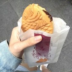 a person holding a sandwich in their hand on the side of the road with other people walking by