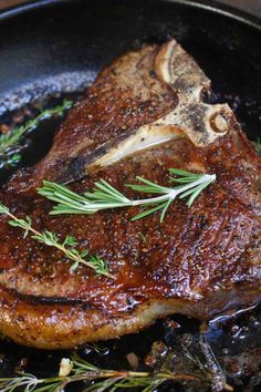 a piece of meat in a skillet with some herbs on the top and bottom